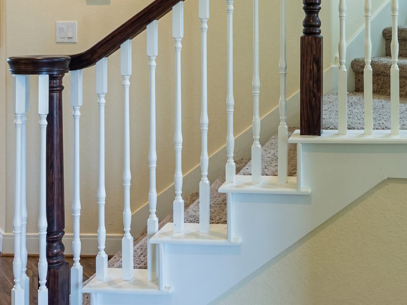 White classic turned wood balusters with a dark stained handrail and newel post on a carpeted stair