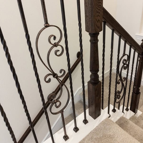 Scroll Series iron balusters with a double scroll design between twisted balusters on a carpeted staircase