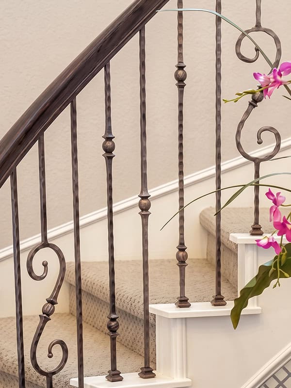 Tuscan Square hand-hammered iron balusters with spheres and scrolls on a carpeted stair