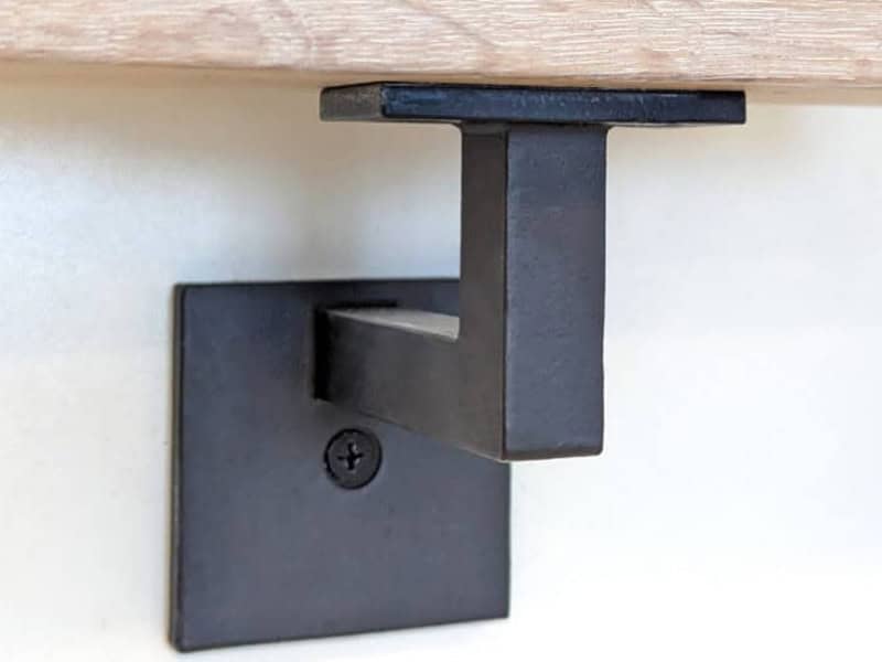 Black wall mount handrail bracket holding a wood handrail