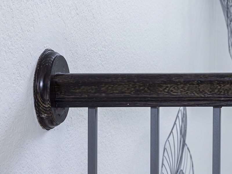 Dark stained wood handrail ending in a round wood rosette mounted to the wall